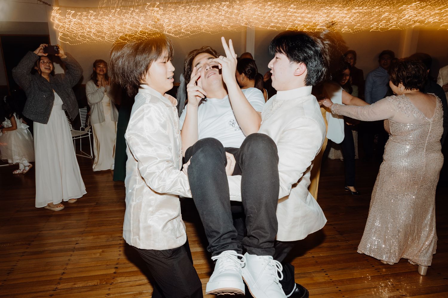 Party guests lifting and carrying someone during an energetic dance celebration.