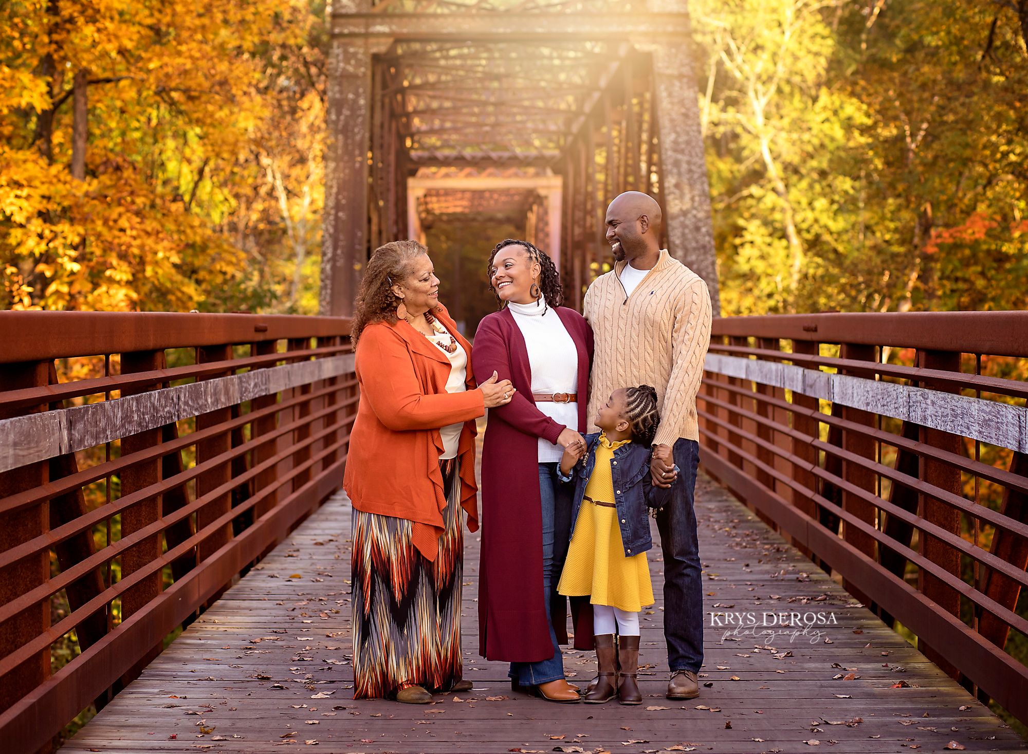 Family standing together on a rustic wooden bridge during autumn with golden foliage surrounding them.
