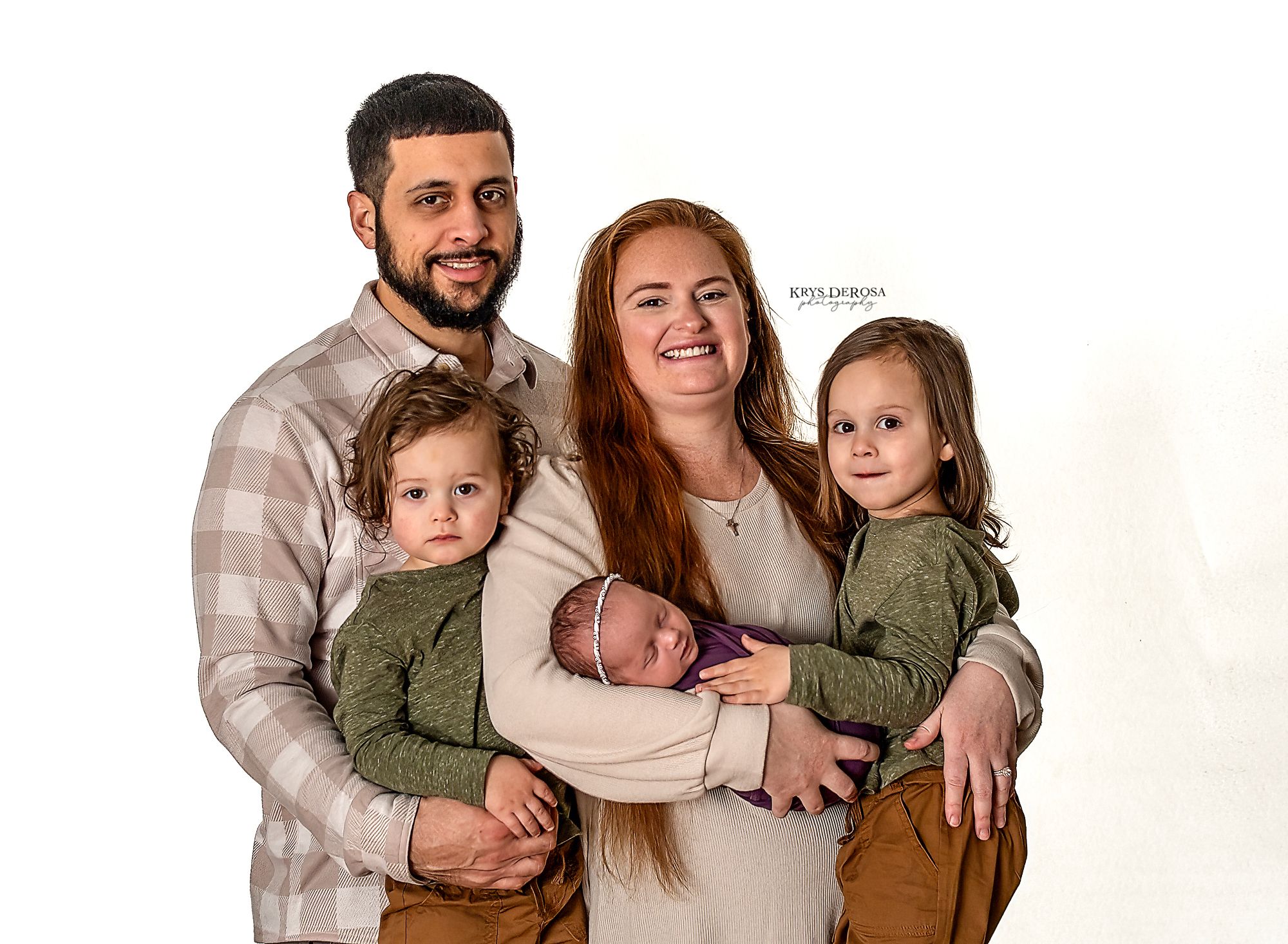 A family of five poses together for a portrait against a white background wearing casual earth-toned clothing.