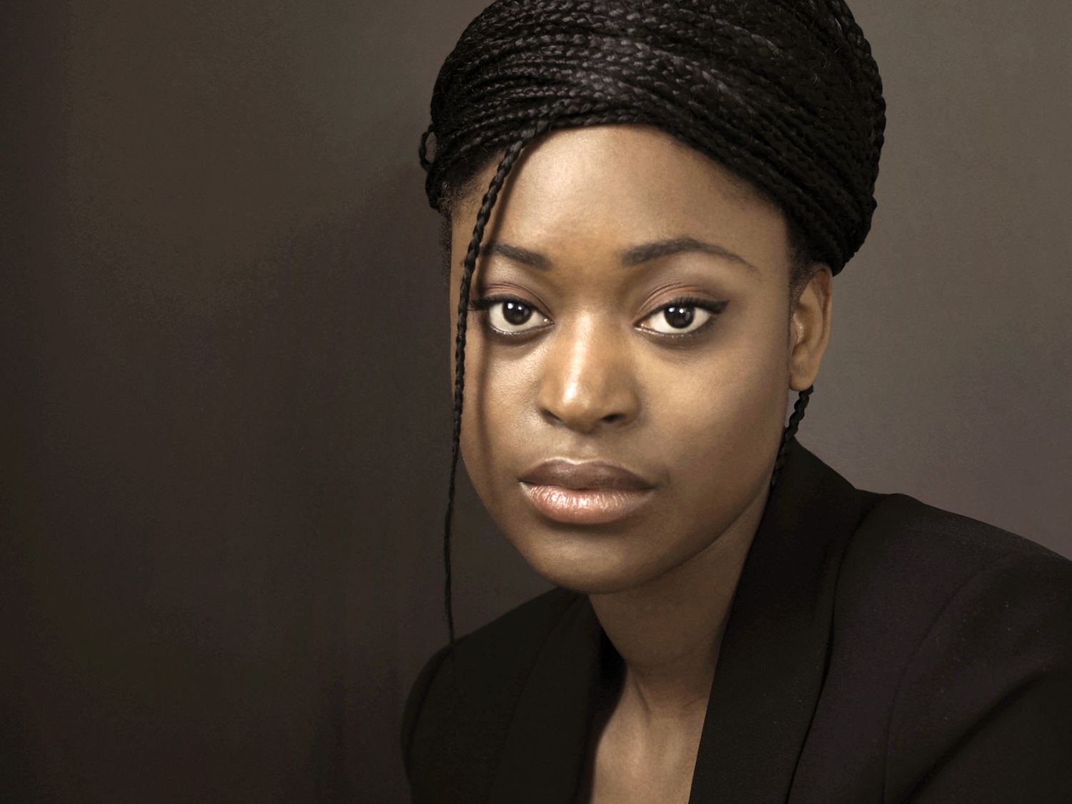 Professional portrait of someone in a black top and head wrap against a dark brown background.
