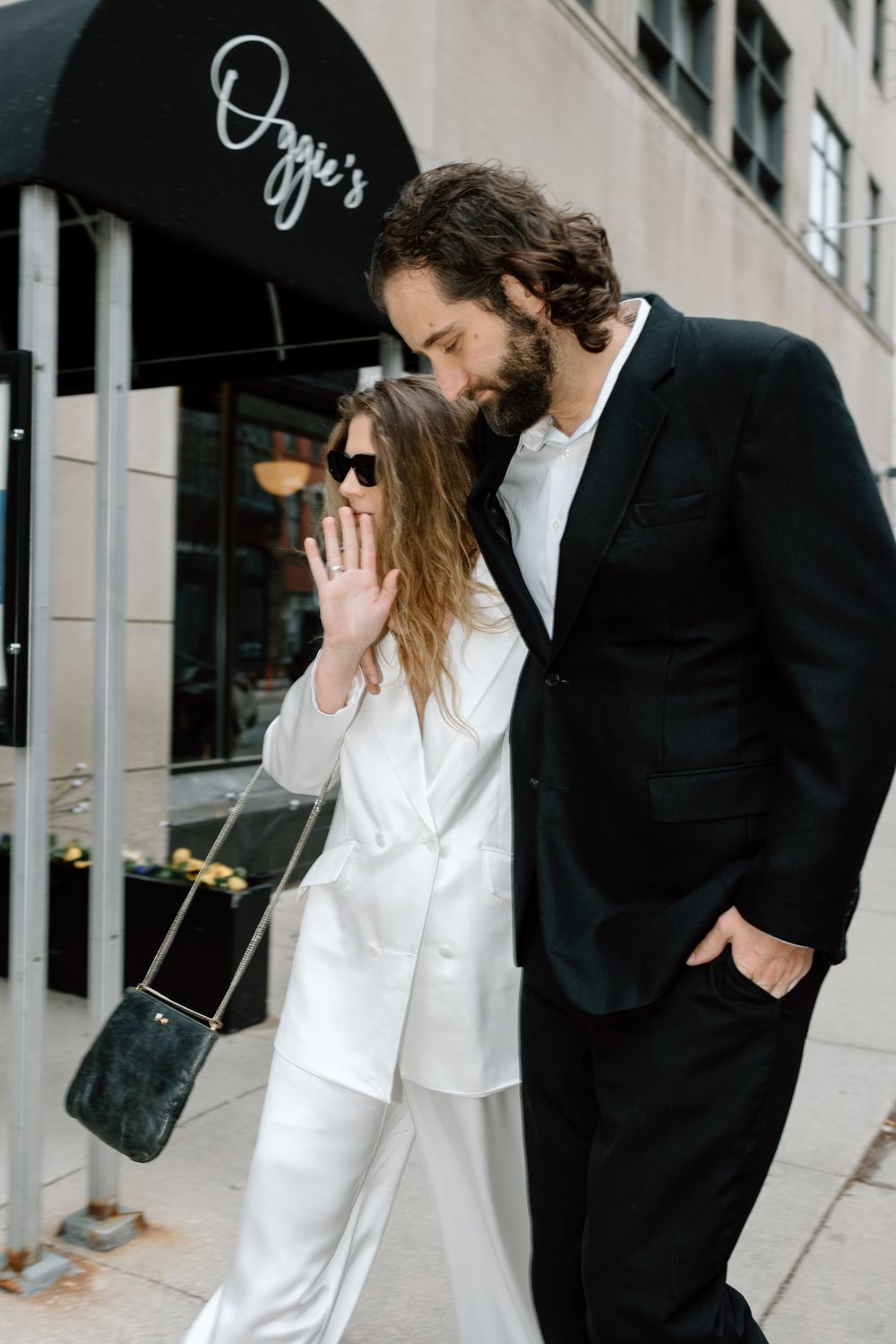 A couple in contrasting black and white outfits shares an intimate moment outside a storefront with Ozzie's signage.