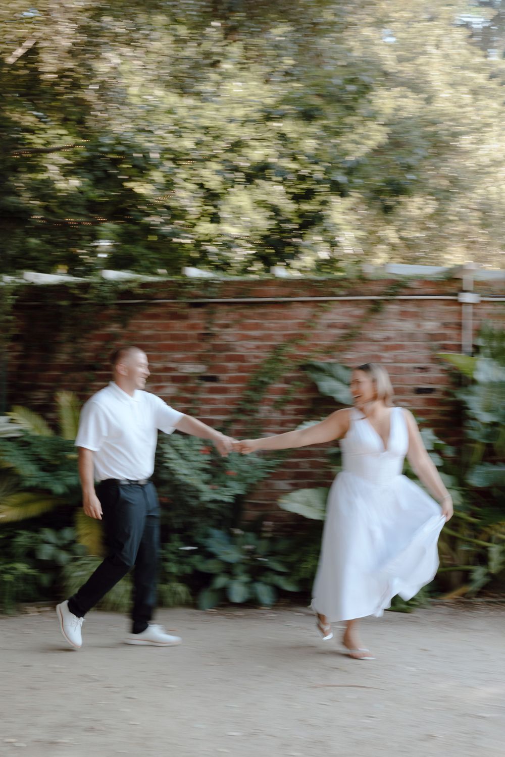 A couple dances playfully against a brick wall covered in lush greenery.