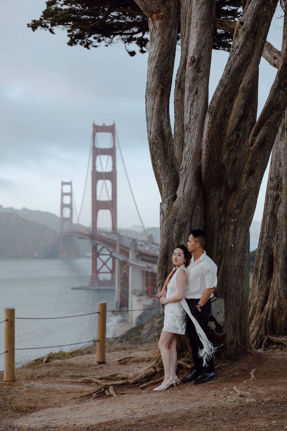 Couple embracing near iconic Golden Gate Bridge on foggy day in San Francisco.