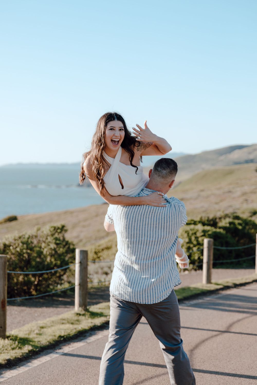 Playful lift pose against scenic coastal hillside backdrop.