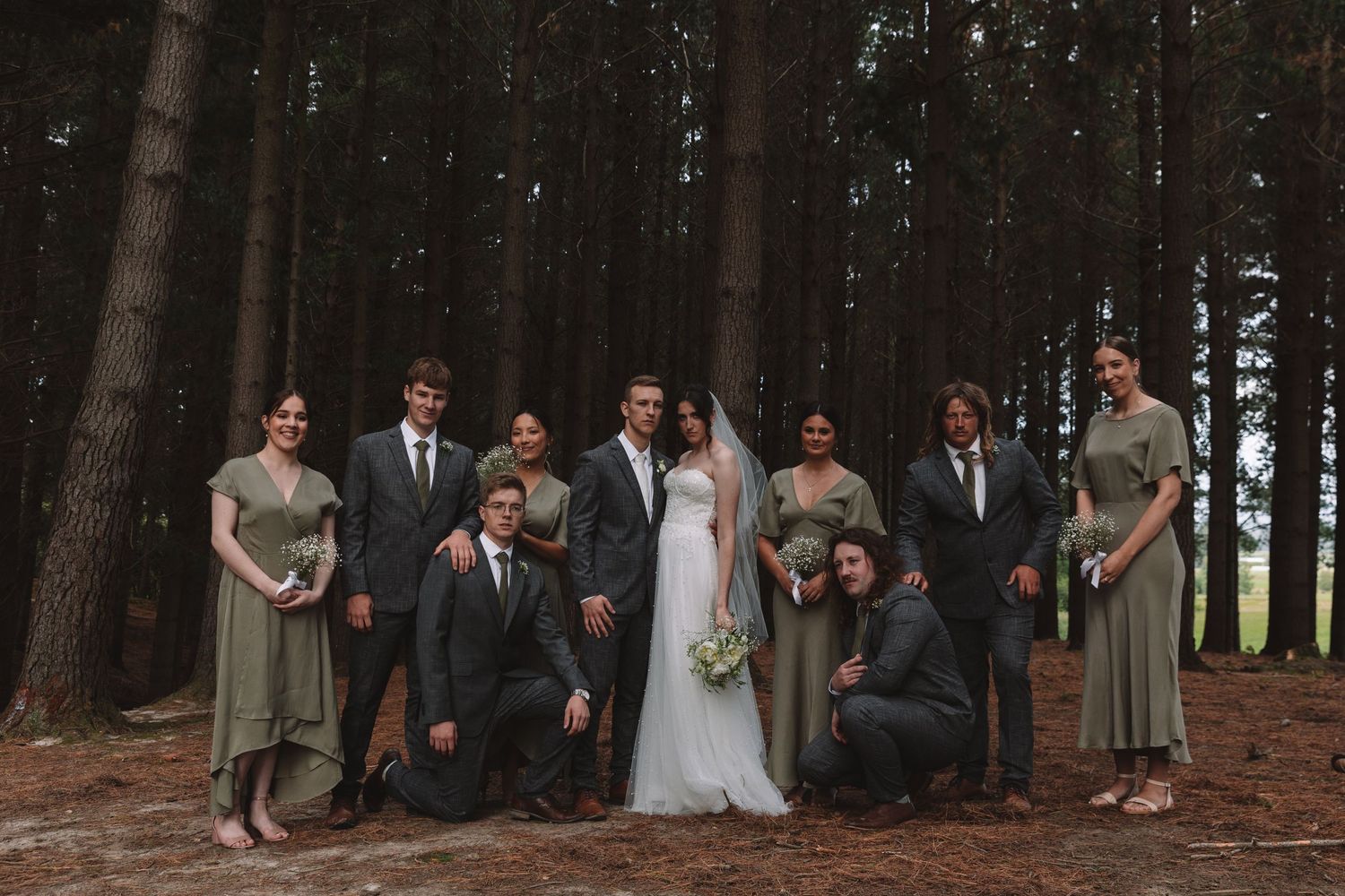 Wedding party poses together in a pine forest setting.