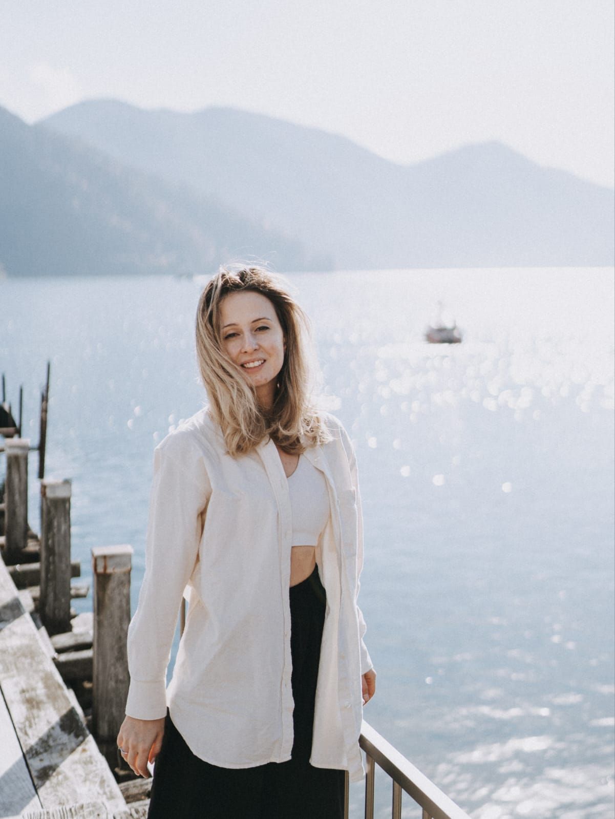 A girl in a white shirt on a pier with mountains in the background
