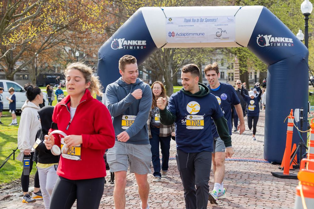 Runners passing through a branded arch during a daytime race event in a park setting.