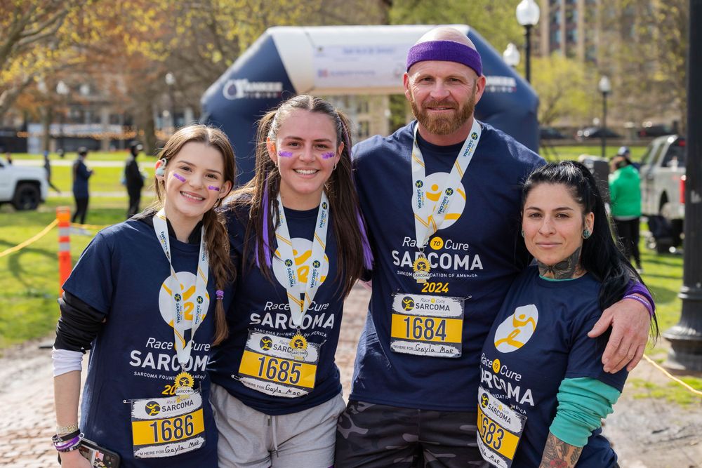 Participants wearing race bibs pose under a branded arch during an outdoor event.
