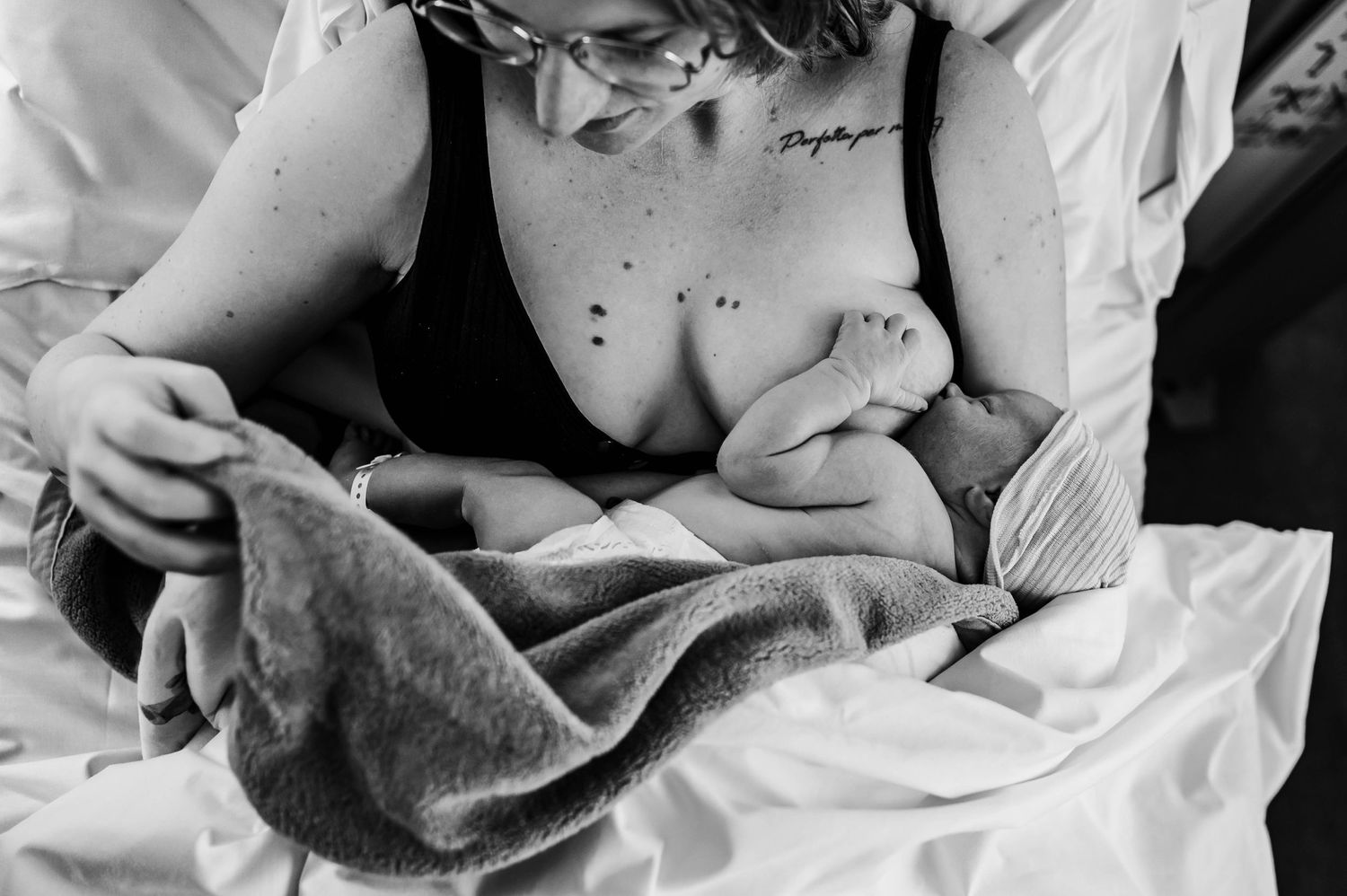 Black and white intimate moment with newborn wrapped in hospital blanket.