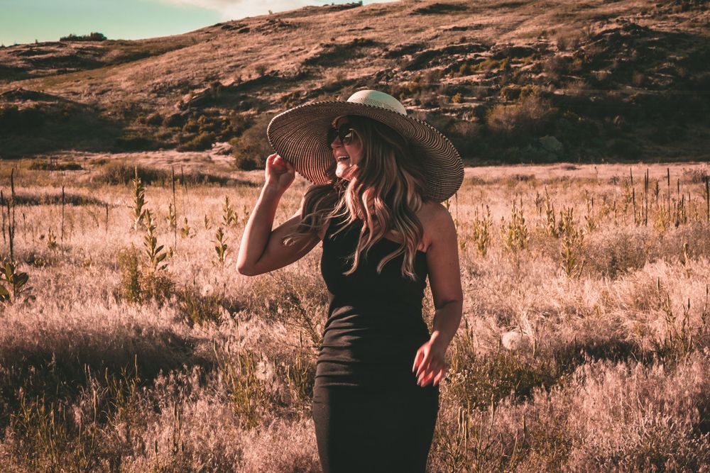 Silhouette in black dress and sun hat against golden desert landscape.