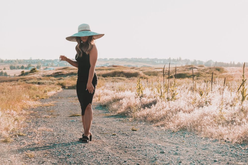 Stylish figure in black dress and mint hat poses on desert path.