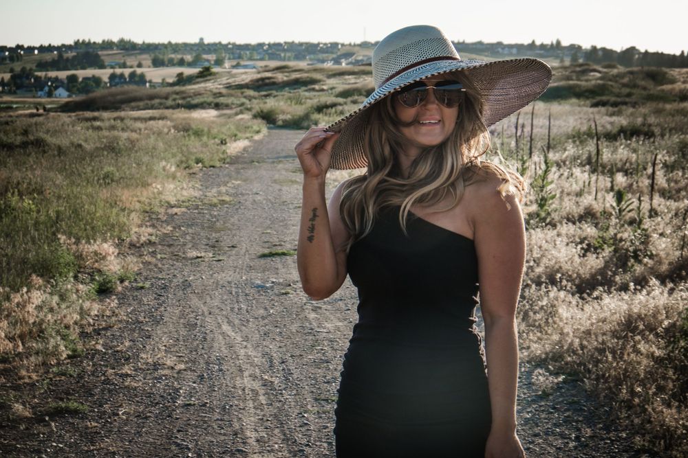 Fashion shot of model in fitted black dress and gray hat on desert path.