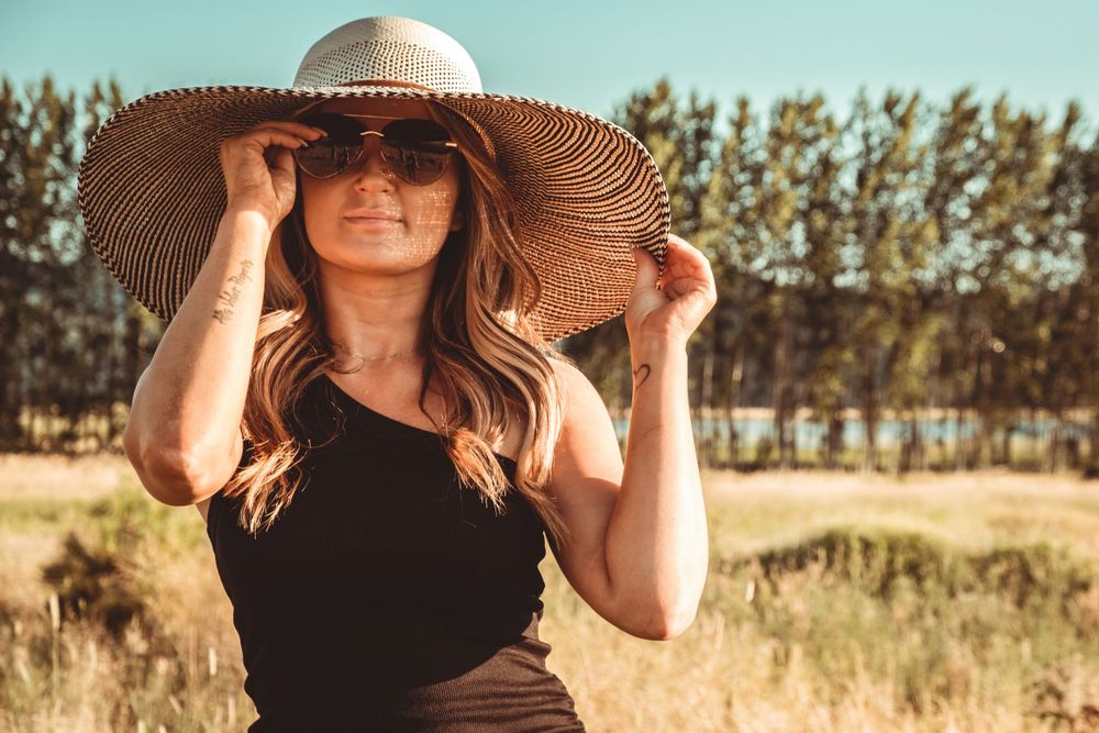 Summer fashion portrait with straw hat against rustic field backdrop.