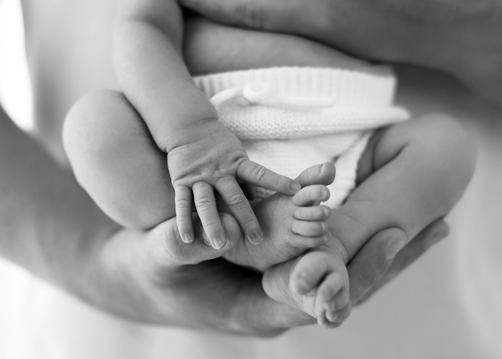 A close-up black and white photo of a person's hands folded together on a light surface.
