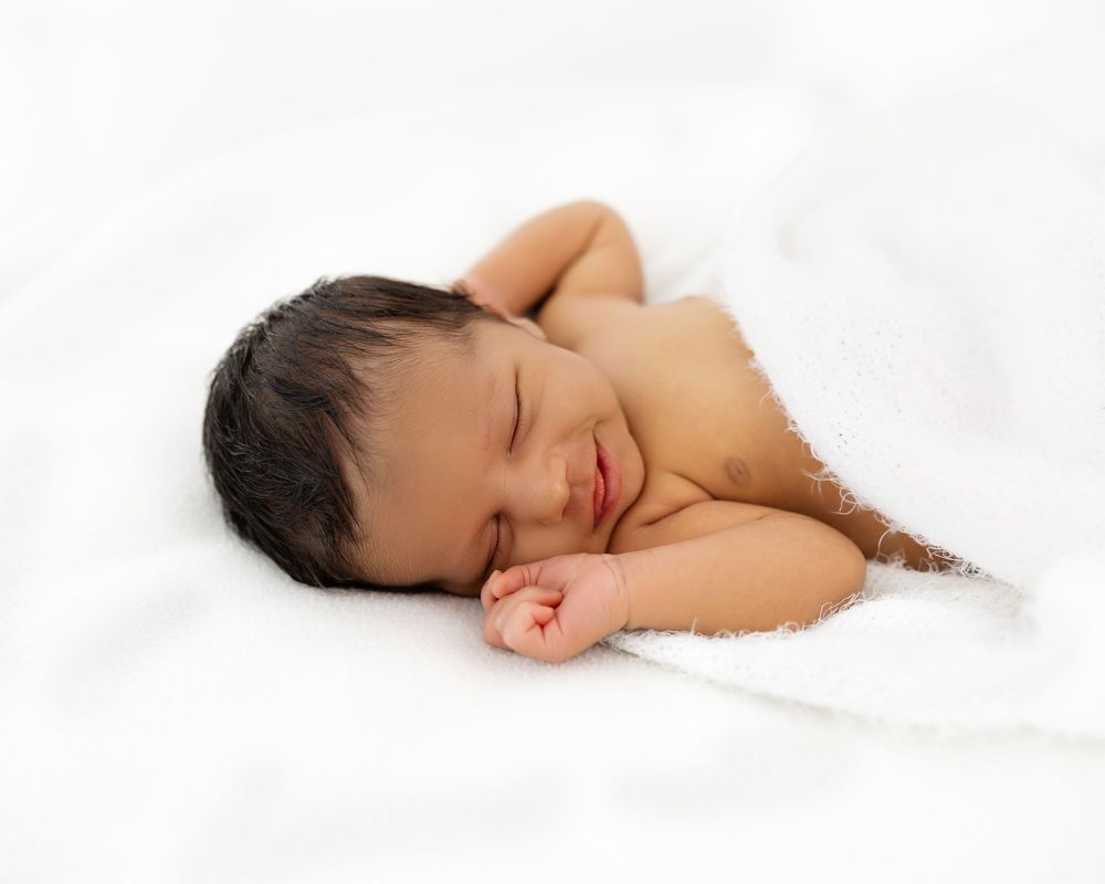 A peaceful sleeping baby nestled in soft white bedding with a gentle smile shows pure contentment and serenity.