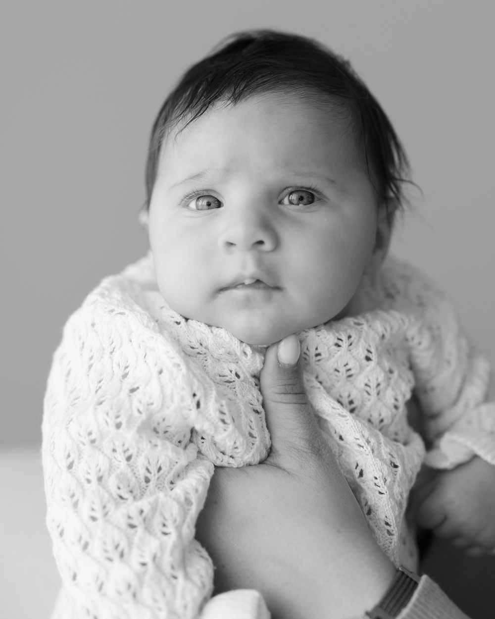 Close up black and white portrait of a baby wearing a delicate white lace dress.