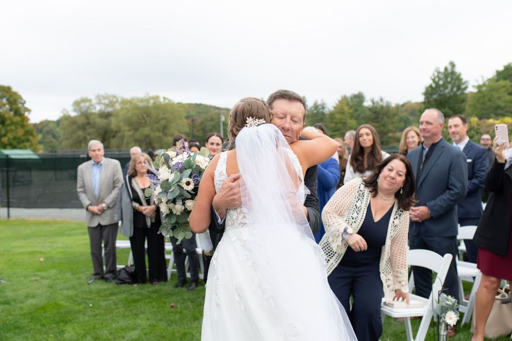 Emotional embrace during outdoor wedding ceremony as guests look on from white chairs.