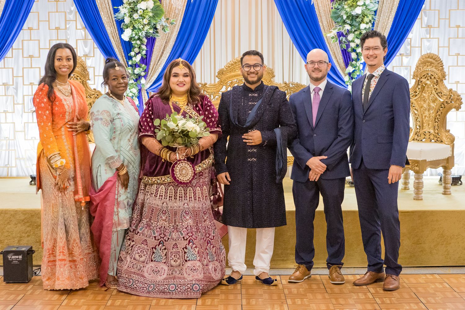 Wedding party group photo with traditional Indian bride in red lehenga and western-dressed attendants.