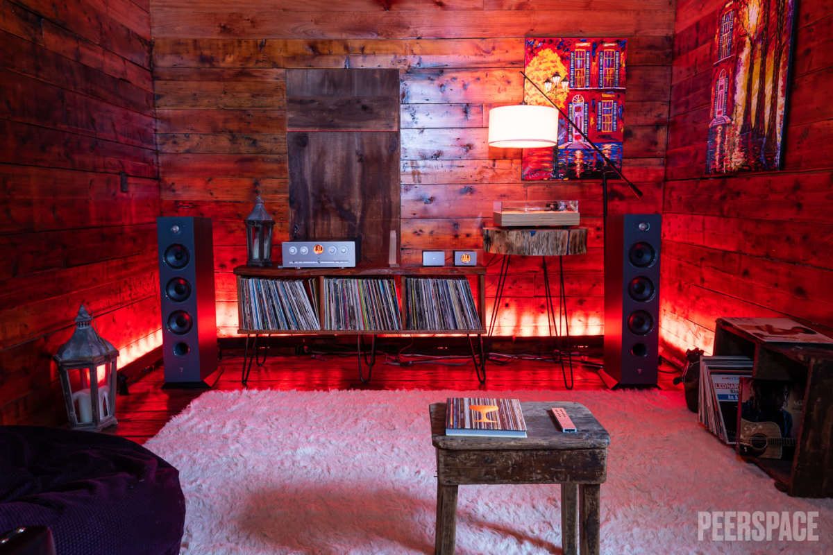 Red-lit music room with vinyl record storage, speakers, and cozy seating area on white carpet.