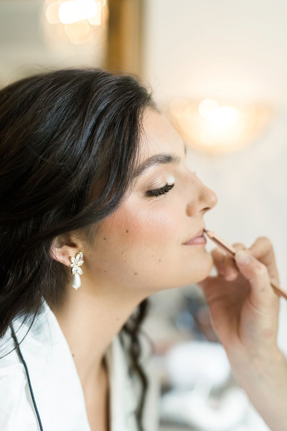 Close-up of bridal makeup application with sparkling earring detail.