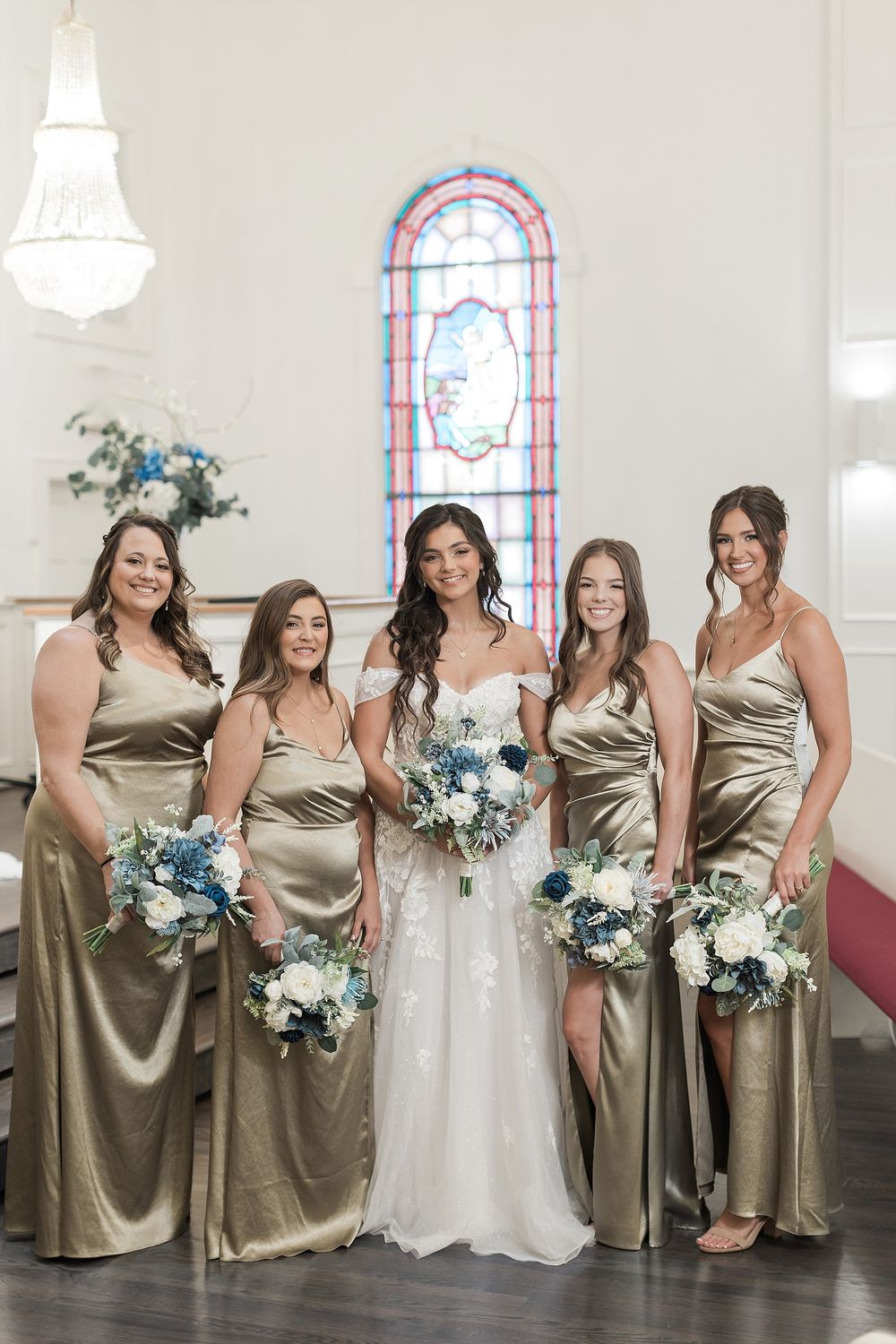 Wedding party poses in church with stained glass window, bridesmaids in champagne satin dresses.