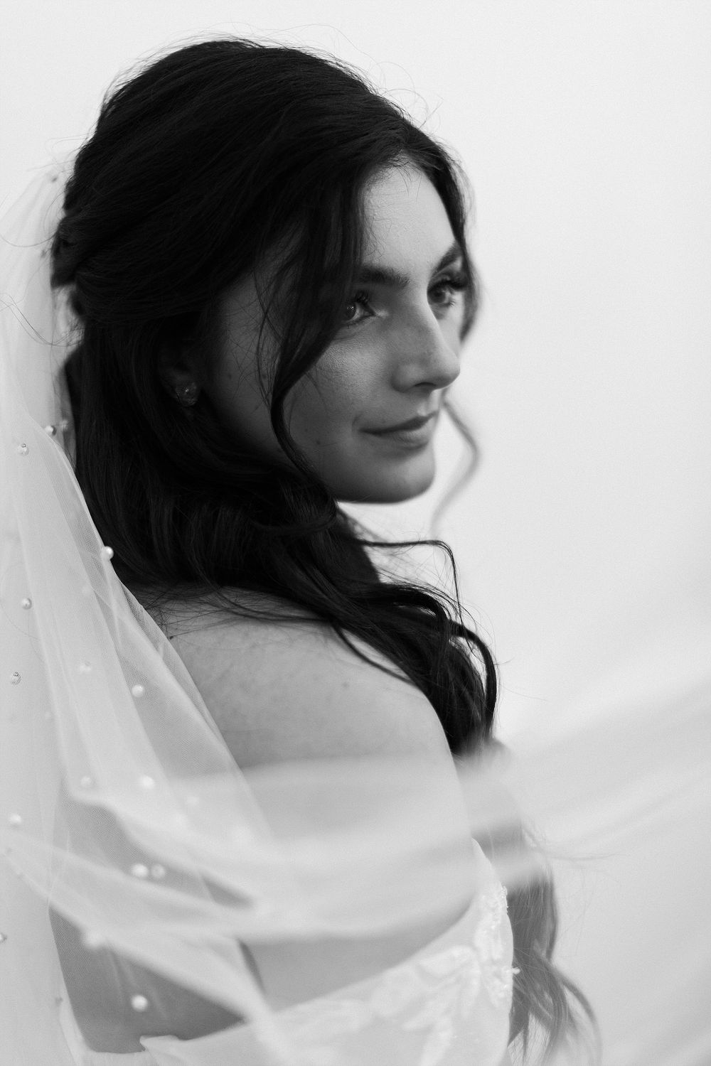 Black and white portrait of bride with flowing veil and dark hair.
