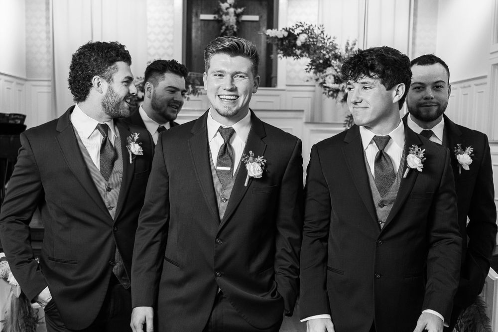 Group of groomsmen in matching dark suits and ties share a candid moment.