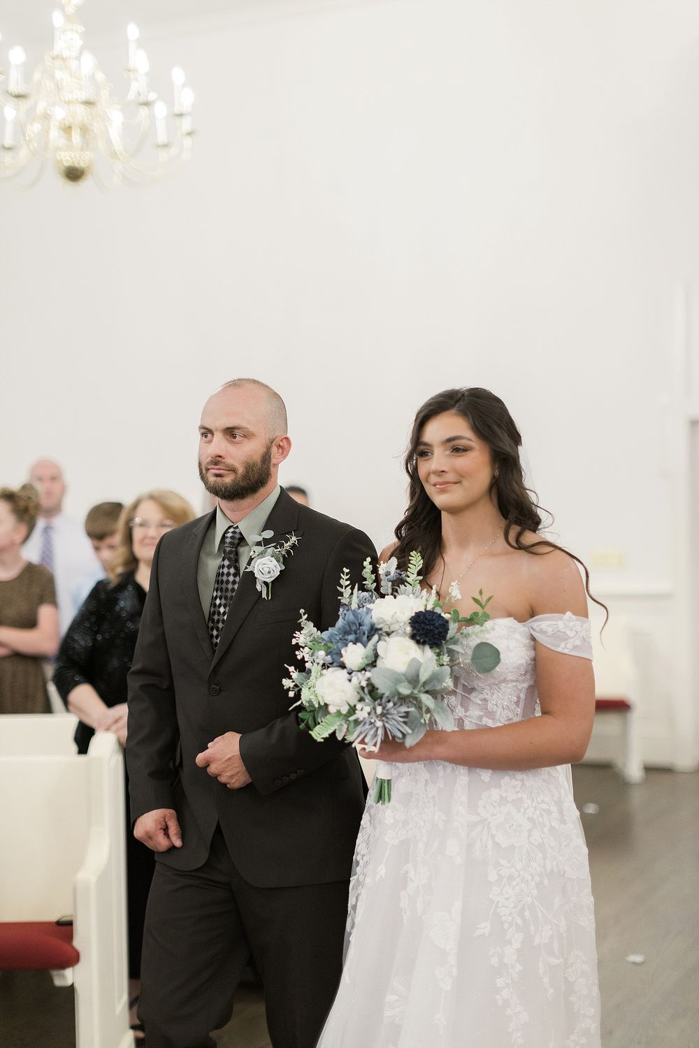 Couple exchanges vows during indoor church ceremony under elegant chandelier.
