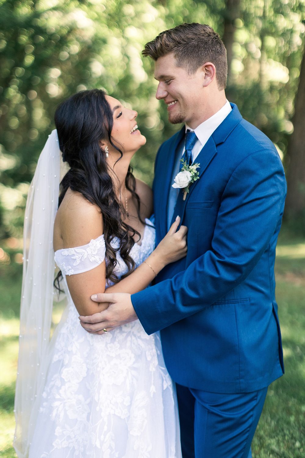 A romantic outdoor wedding portrait with couple embracing in front of lush greenery.