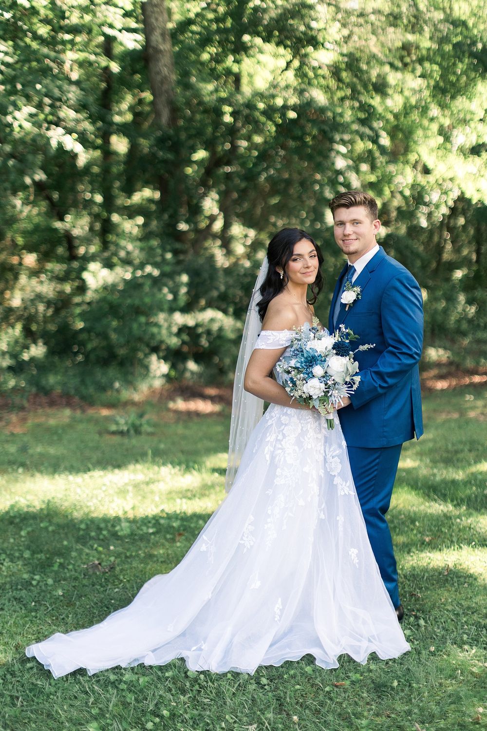 Elegant outdoor wedding portrait with bride holding blue bouquet and groom in navy suit.