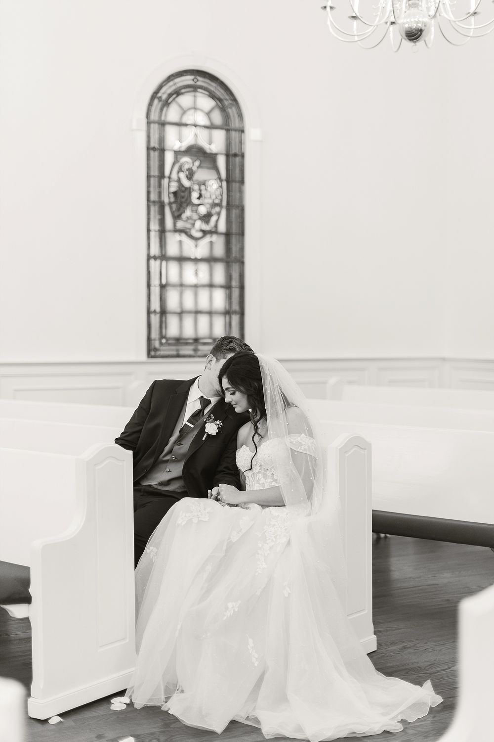 Black and white church wedding photo with stained glass window and couple sharing quiet moment.