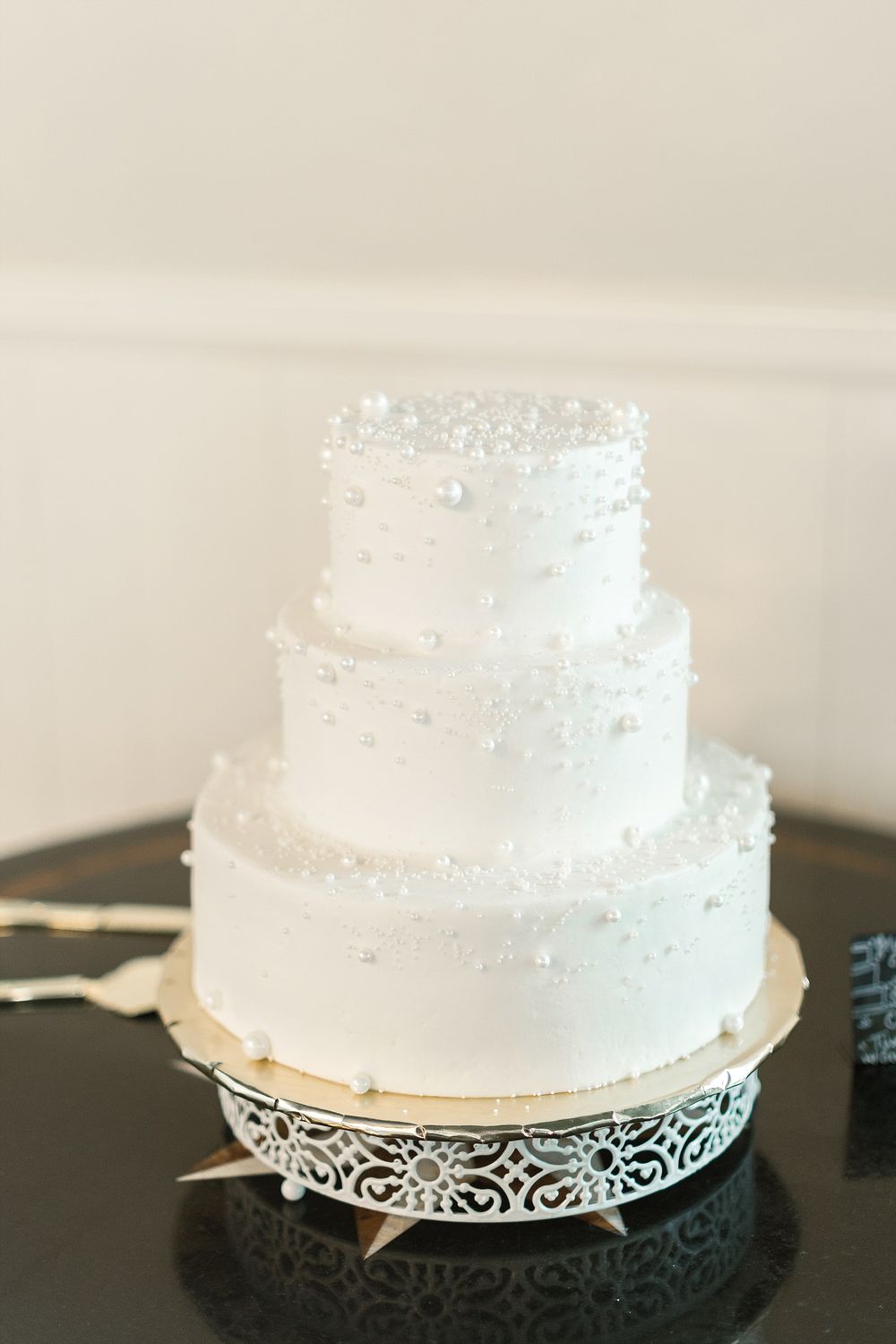 Elegant three-tiered white wedding cake with delicate pearl details displayed on an ornate silver stand.