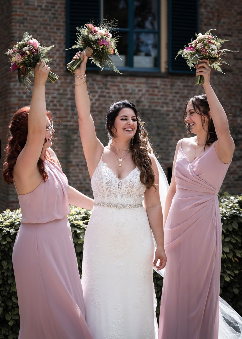 Bruiloftsfoto van bruid met bruidsmeisjes houden bloemen omhoog tijdens huwelijksdag vastgelegd bij trouwlocatie Kasteel Wijenburg Echteld.