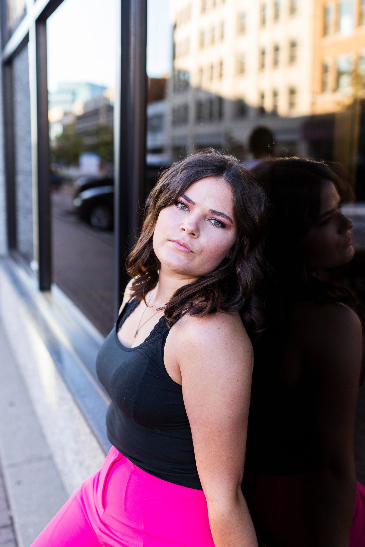 Senior leaning against a dark glass window with a serious expression looking at the camera. Captured by Shania Hirdler P