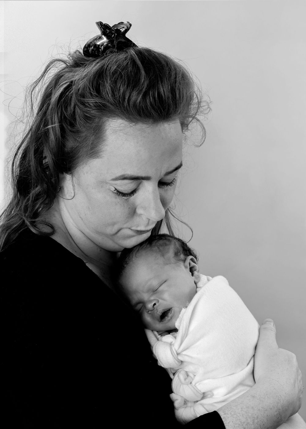 Black and white portrait showing tender moment between parent and sleeping newborn.