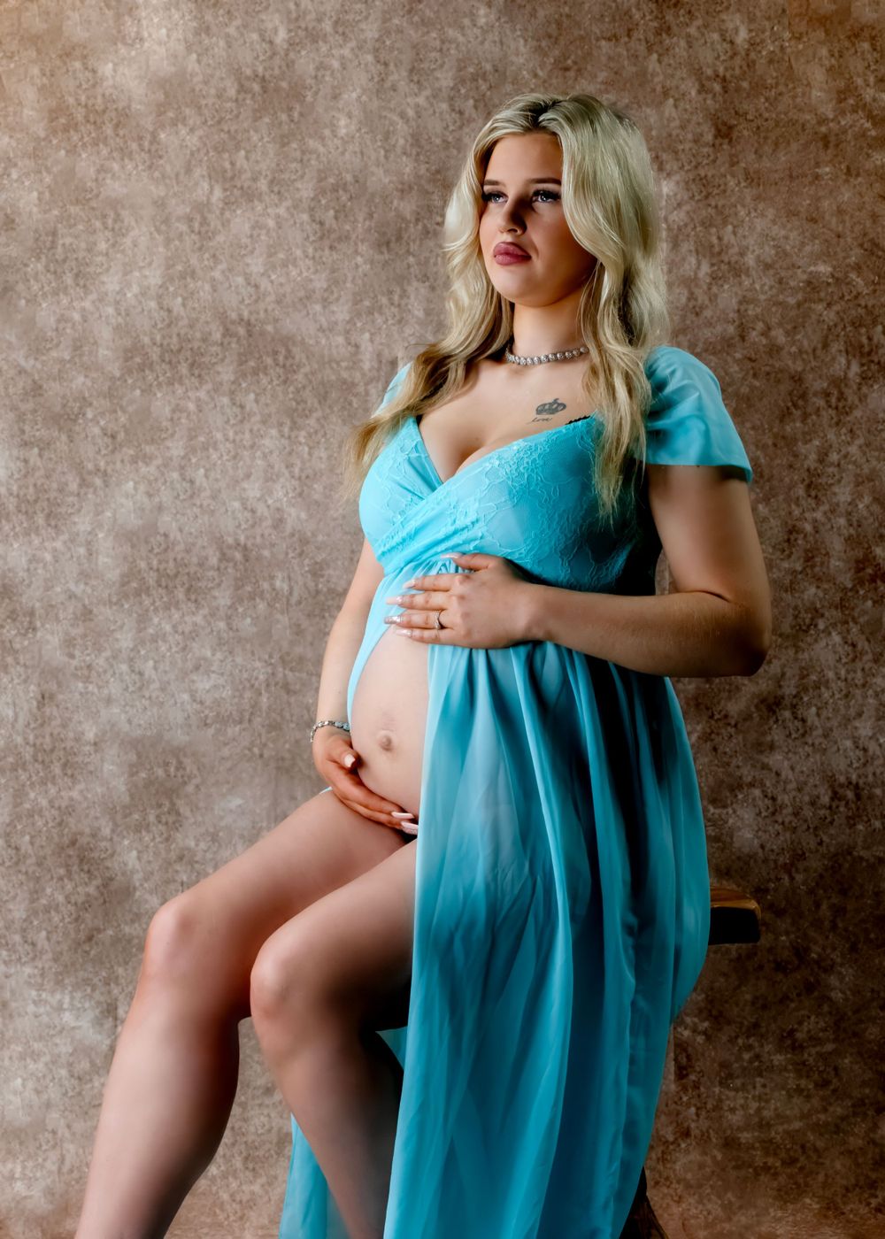 Maternity portrait in turquoise dress with short sleeves against textured background.