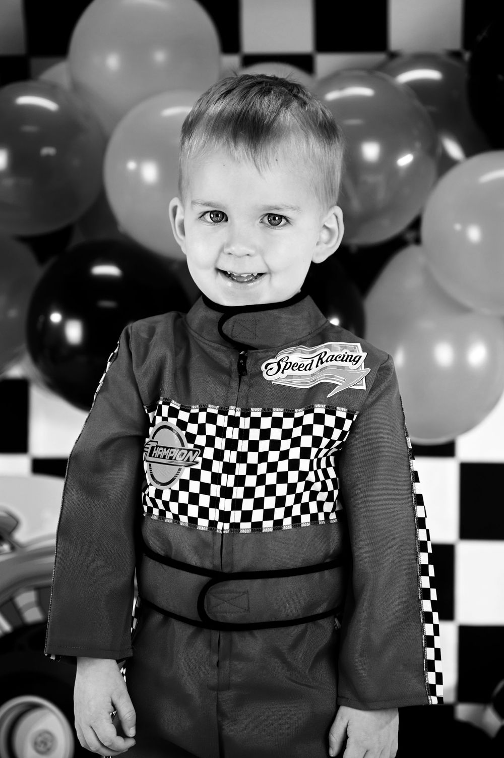 Black and white portrait with checkered racing outfit against balloon backdrop.
