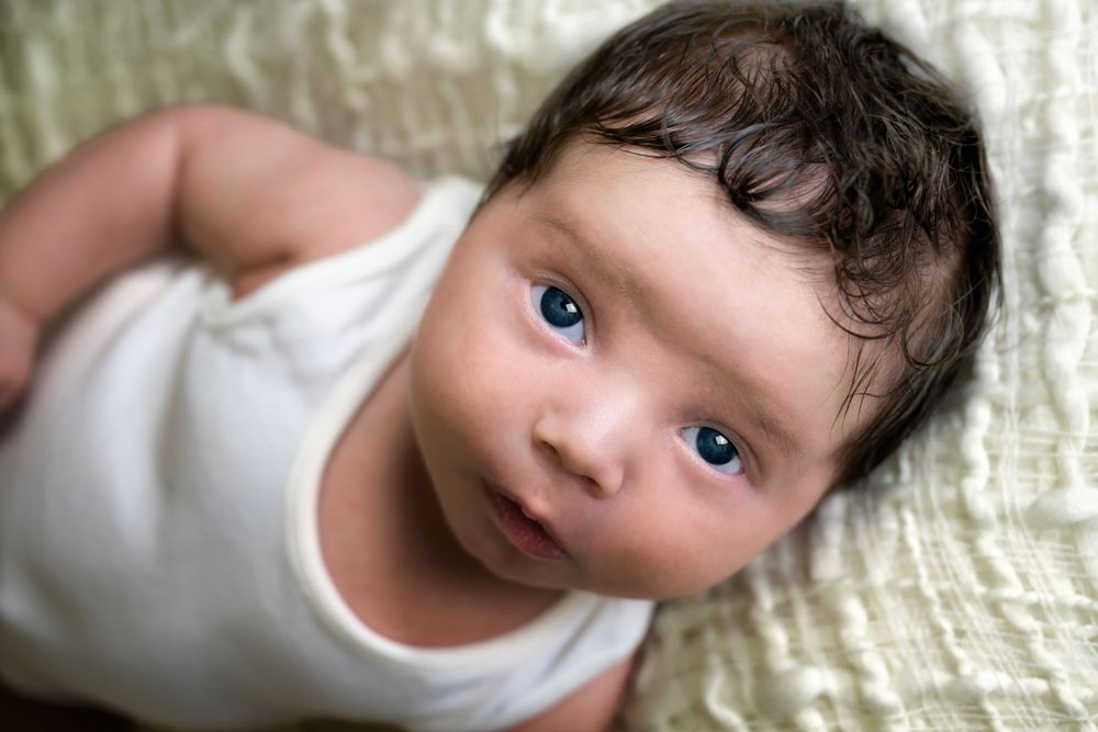 Close-up portrait of baby in white outfit against cream textured background.