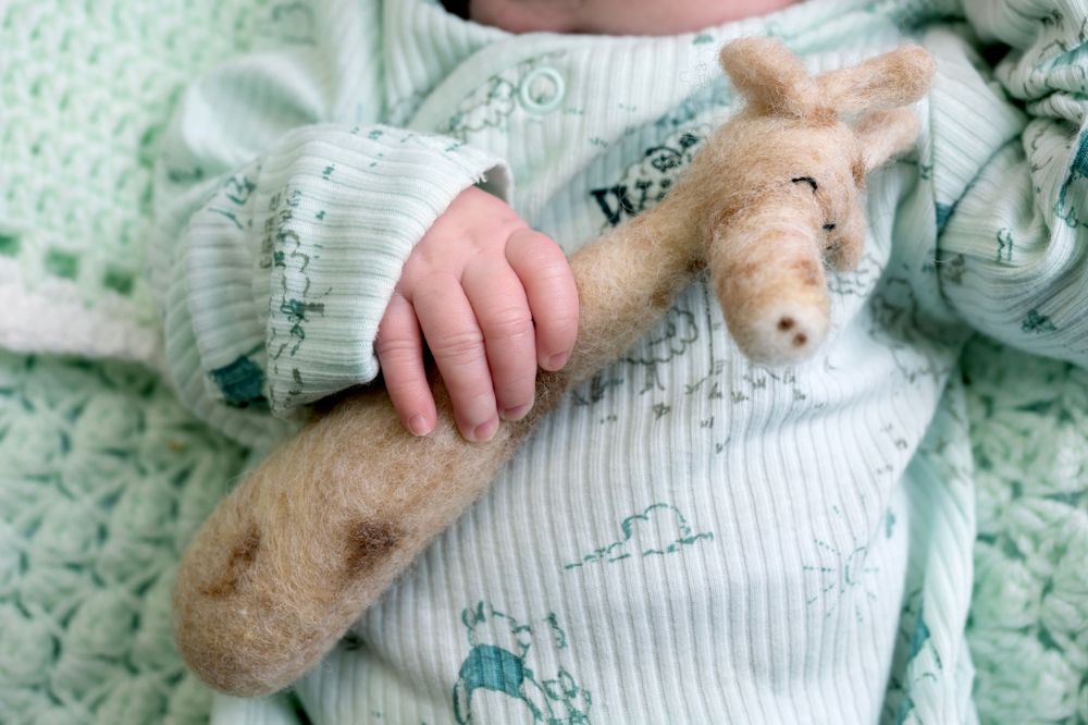 Close-up of small hand holding plush toy against mint green knitted blanket.