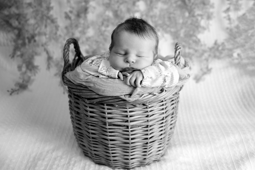 Black and white portrait of sleeping baby in woven basket.