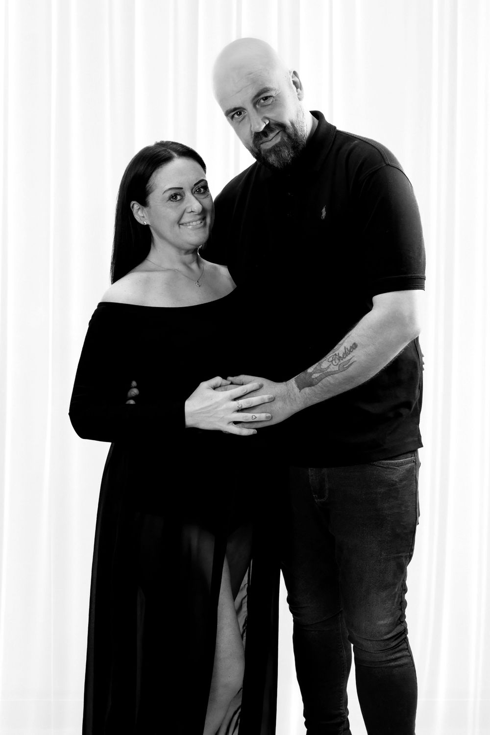Black and white maternity portrait of couple in coordinated dark outfits.