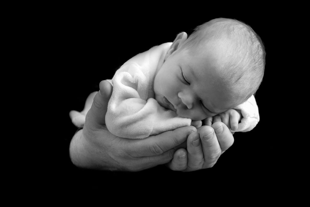 Black and white photo of a sleeping newborn baby cradled in gentle hands.