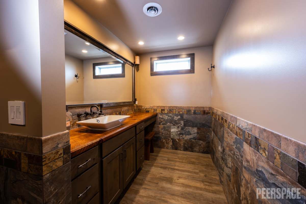 Modern bathroom interior with wooden vanity, stone accent wall and hardwood flooring.