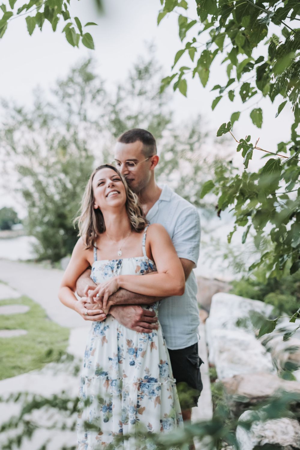 An engaged couple hugs and laughs along the Hudson River