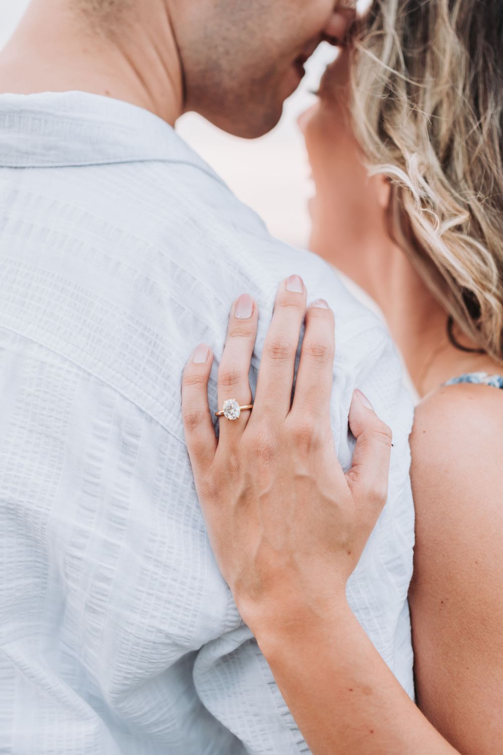 Close-up shot of a person wearing an engagement ring and white shirt embracing another in romantic pose.