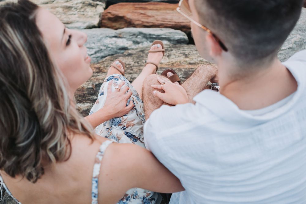 An engaged couple sits together on a rock wall along the Hudson River
