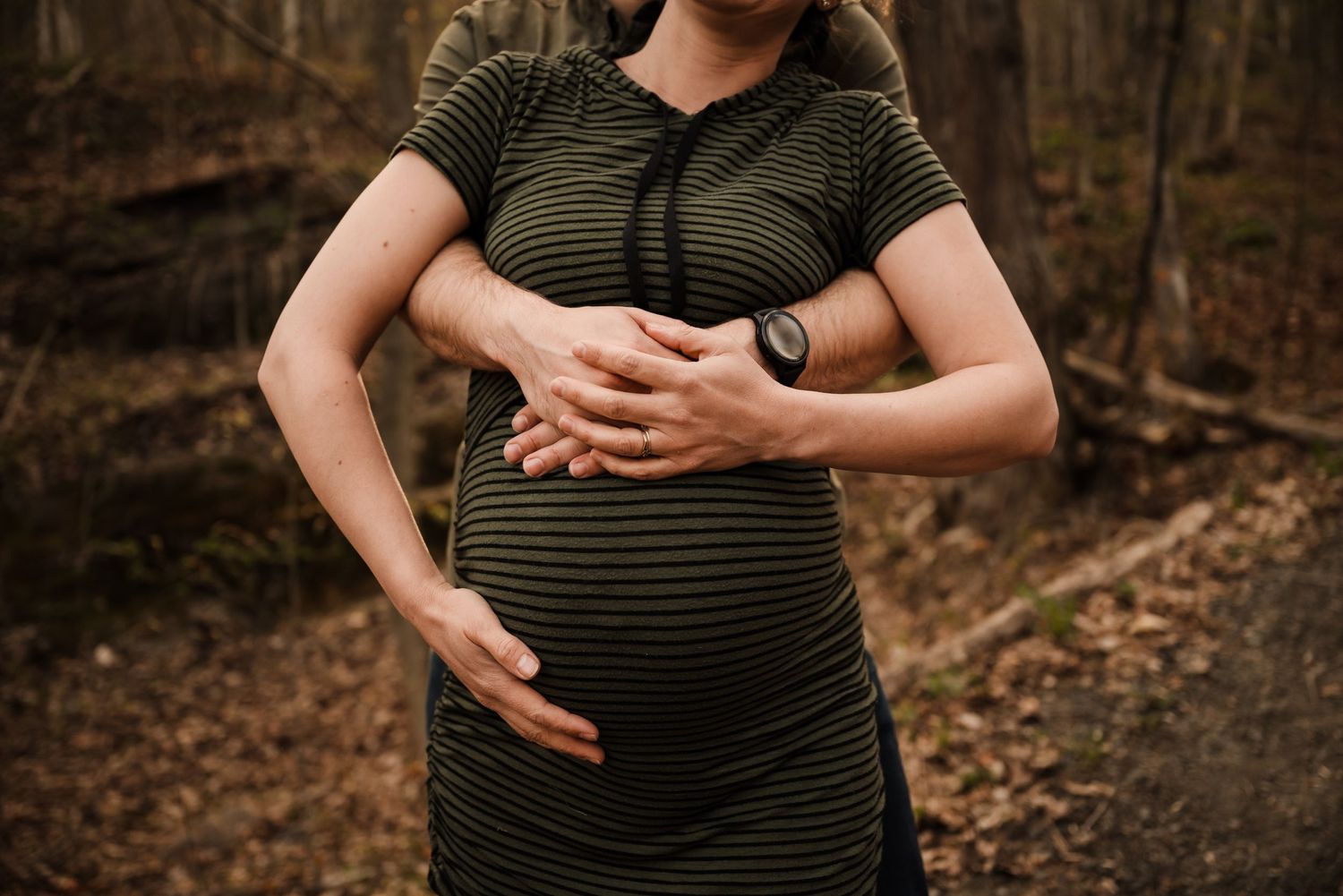 Person in striped dress holding growing baby bump against forest backdrop.
