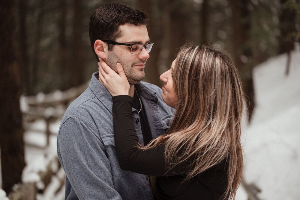 An intimate moment between a couple sharing an embrace in a snowy forest setting.