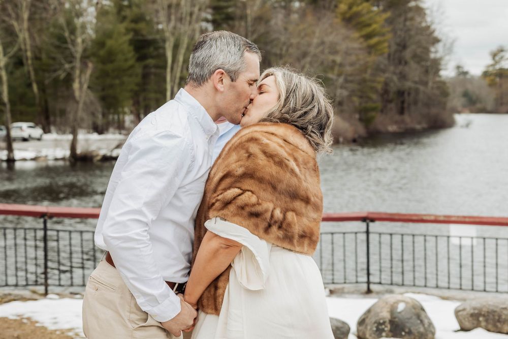 An intimate winter wedding kiss on a lakeside deck with the bride wearing a brown fur stole.