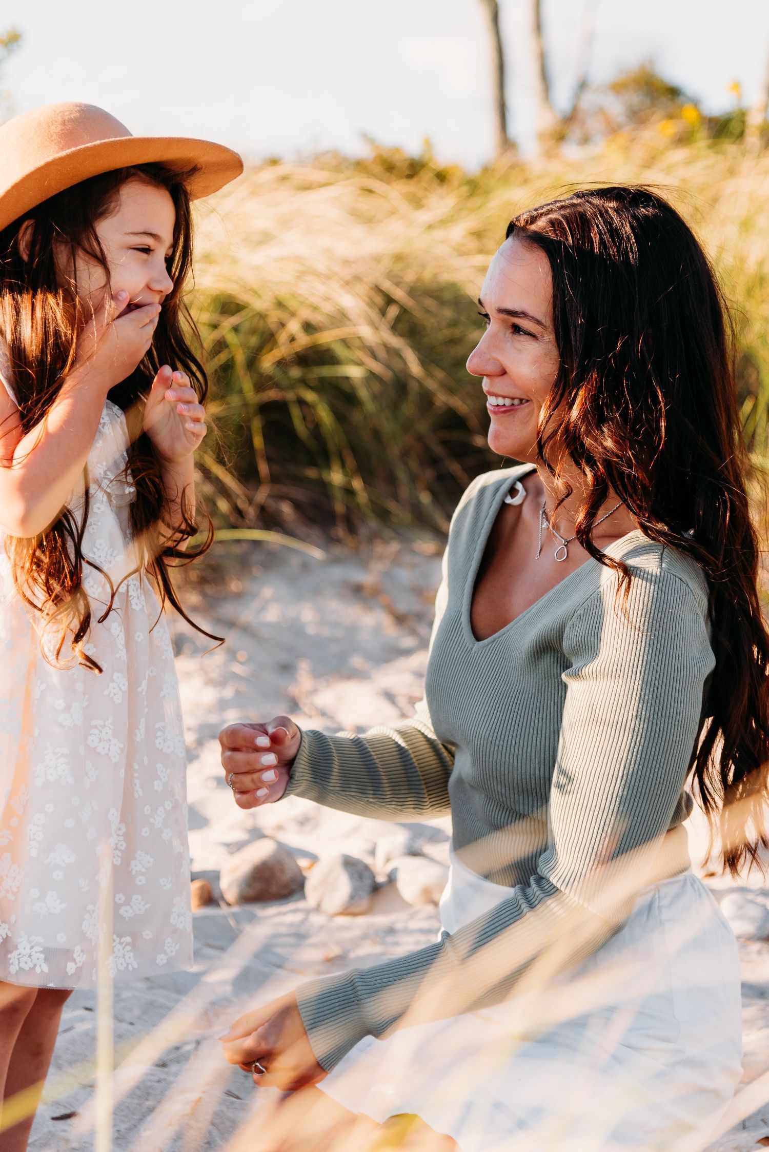 A joyful moment shared between two people laughing together on a sunny beach with tall grass in the background.